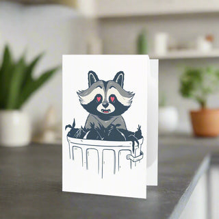 Front of greeting card with illustrated raccoon leaning over dumpster