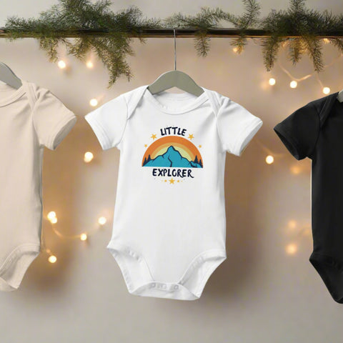 White and black Little Explorer baby onesies hanging on wooden rack