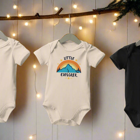 Organic cotton Little Explorer baby onesie hanging between lights on wooden backdrop