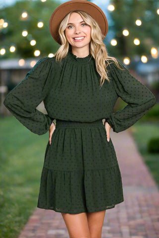 Woman wearing forest green swiss dot mini dress with smocked neck and long sleeves