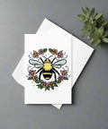 Bee and floral wreath greeting card displayed with white envelope