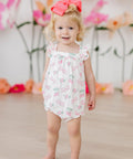 Baby girl wearing pink berry & bow print ruffle cross-back romper, front view