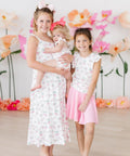 Baby girl wearing pink berry & bow print ruffle cross-back romper, siblings wearing similar styles in same print.
