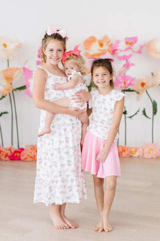 Baby girl wearing pink berry & bow print ruffle cross-back romper, siblings wearing similar styles in same print.