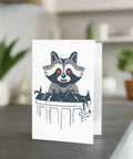  Front of greeting card with illustrated raccoon leaning over dumpster