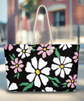 Black oversized tote bag with white and pink daisy flowers and cream rope handles on city sidewalk