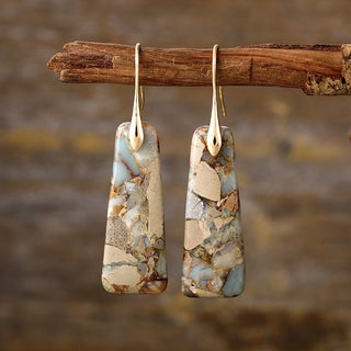 Handcrafted natural stone drop earrings with gold-plated accents, hanging from a rustic wooden branch.