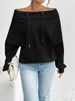 Woman wearing a black off-shoulder drawstring long sleeve top styled with jeans