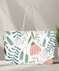 Oversized canvas tote bag with playful pink and green floral print against a sunlit wall