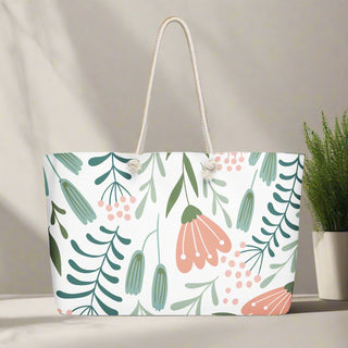 Oversized canvas tote bag with playful pink and green floral print against a sunlit wall