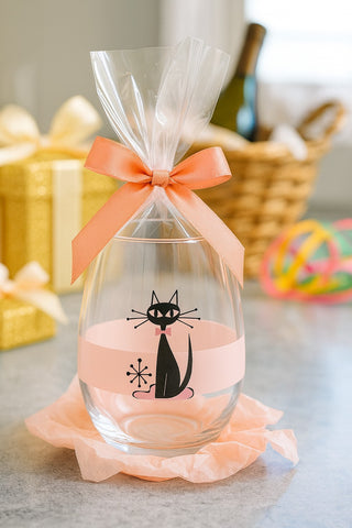 Decorative glass bottle with a black cat design and pink ribbon on a table.