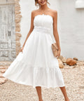 Woman wearing strapless smocked white midi dress with flowy skirt styled with clutch