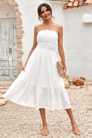 Woman wearing strapless smocked white midi dress with flowy skirt styled with clutch