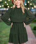 Woman wearing forest green swiss dot mini dress with smocked neck and long sleeves