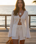 Woman wearing a white tie front cover-up and matching shorts set while walking along the beach at sunset.