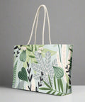 Large canvas travel tote bag featuring green jungle leaves and white tropical foliage

