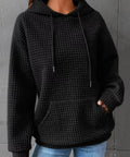 Woman in black waffle knit pullover hoodie, hands in pockets