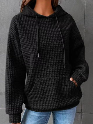 Woman in black waffle knit pullover hoodie, hands in pockets