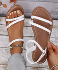 Close-up of white strappy flat sandals featuring a cushioned footbed and adjustable ankle strap.